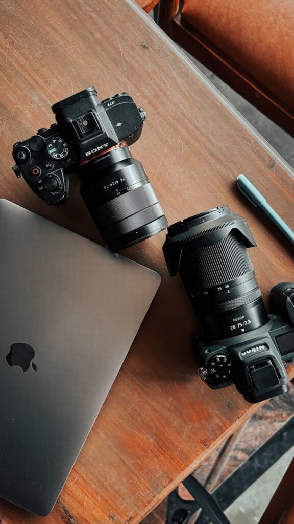 Top view of professional cameras and a laptop on a wooden desk, showcasing photography equipment.