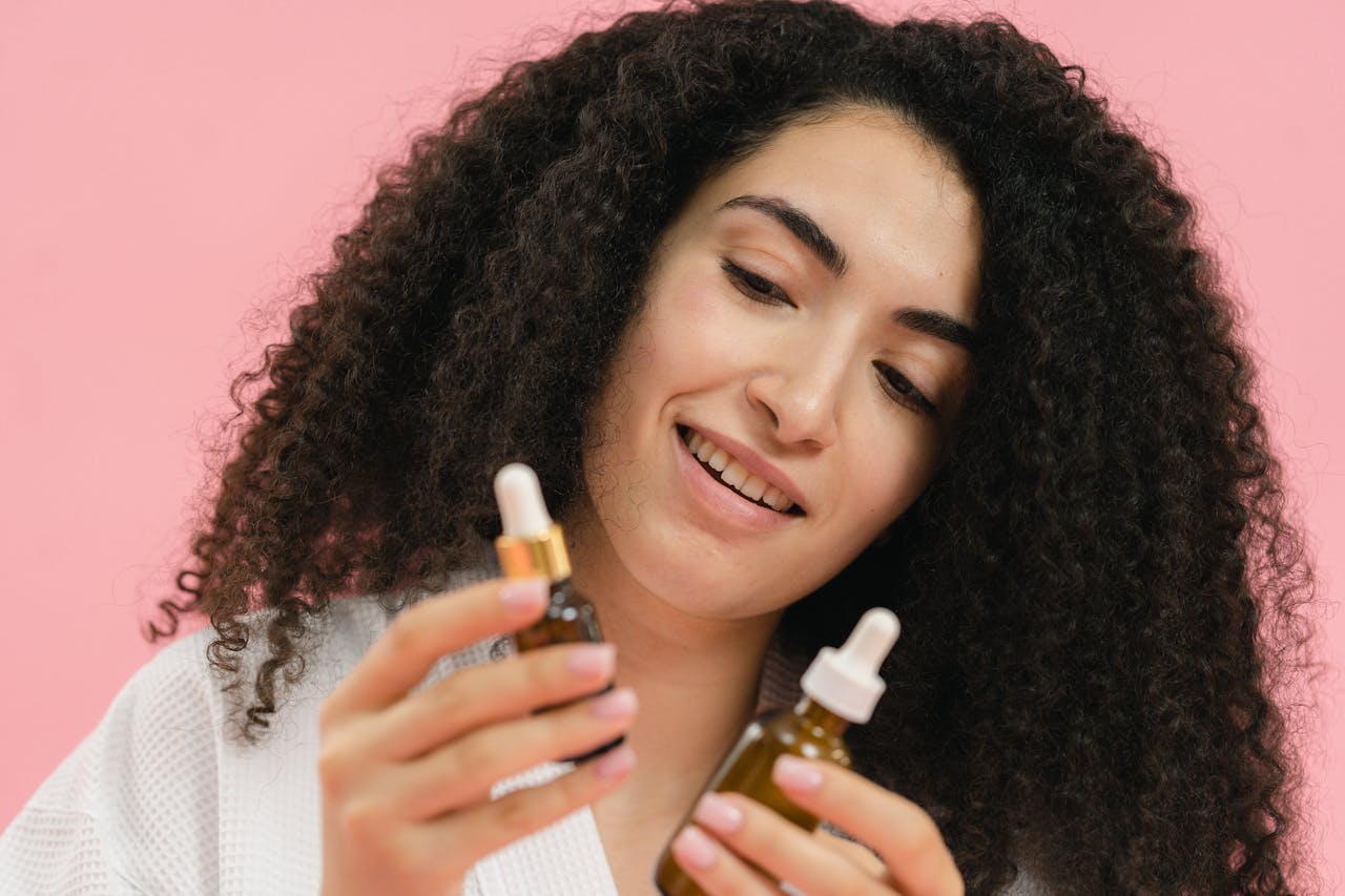 A young woman analyzes skincare bottles, set against a pink backdrop.